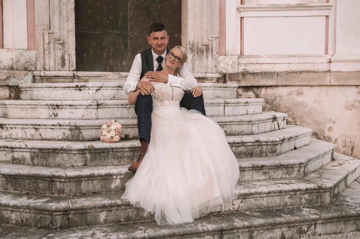 Poročni par v Novem mestu na Dolenjskem; sproščena poza v zelenem parku in mehka naravna svetloba ustvarita miren, brezčasen vtis po obredu.